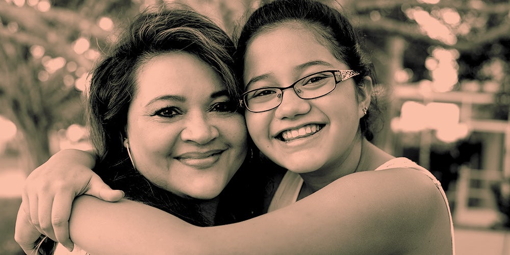 Mom and daughter hugging, smiling, and looking camera
